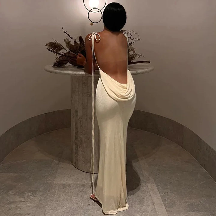 Woman in a long, flowing dress standing in a room with a table and decorative elements.
