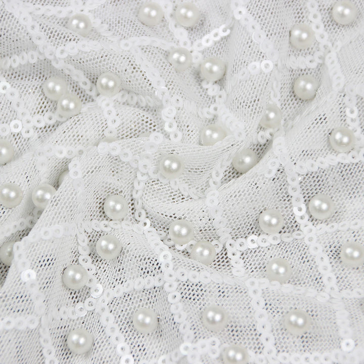 Woman in a stylish white outfit with embellishments standing on a city street.