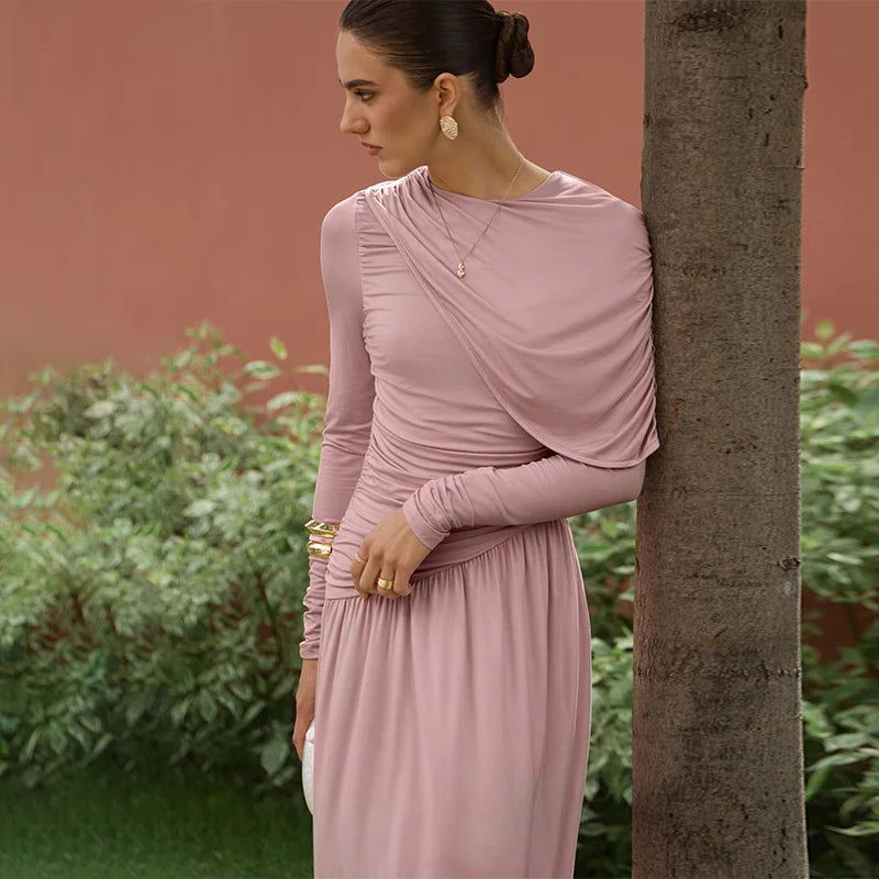 Woman in a pink dress leaning against a tree with a blurred background