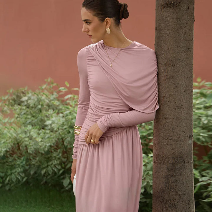 Woman in a pink dress leaning against a tree with a blurred background