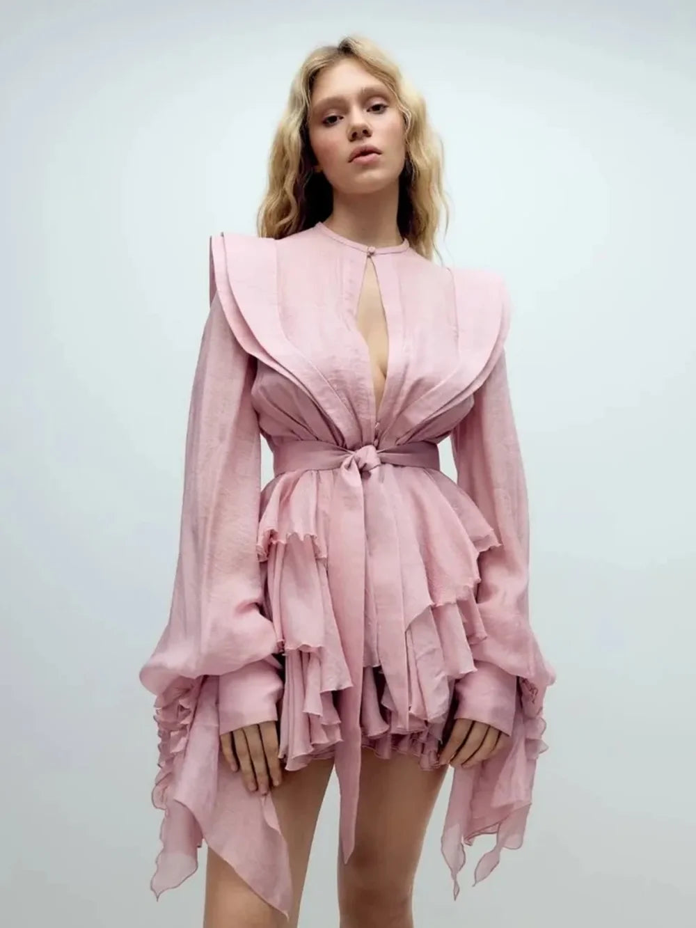 Woman wearing a pink dress with long sleeves and ruffled layers on a white background