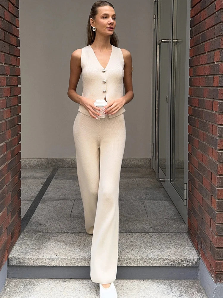 Woman in a beige outfit standing in an urban setting with brick walls.