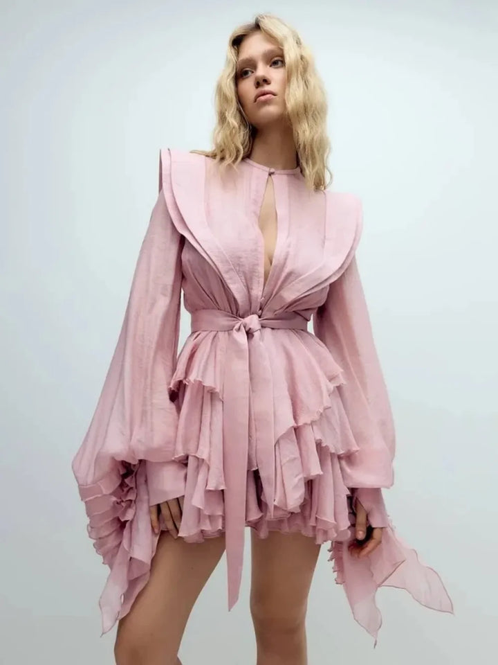 Woman wearing a pink dress with long sleeves and ruffled layers on a light gray background