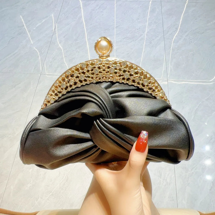 Black clutch with gold embellishments held by a hand against a light background