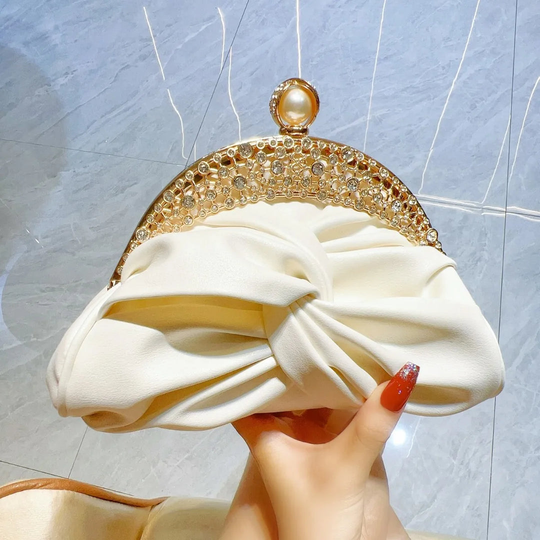 White clutch bag with gold embellishments held by a hand against a light background