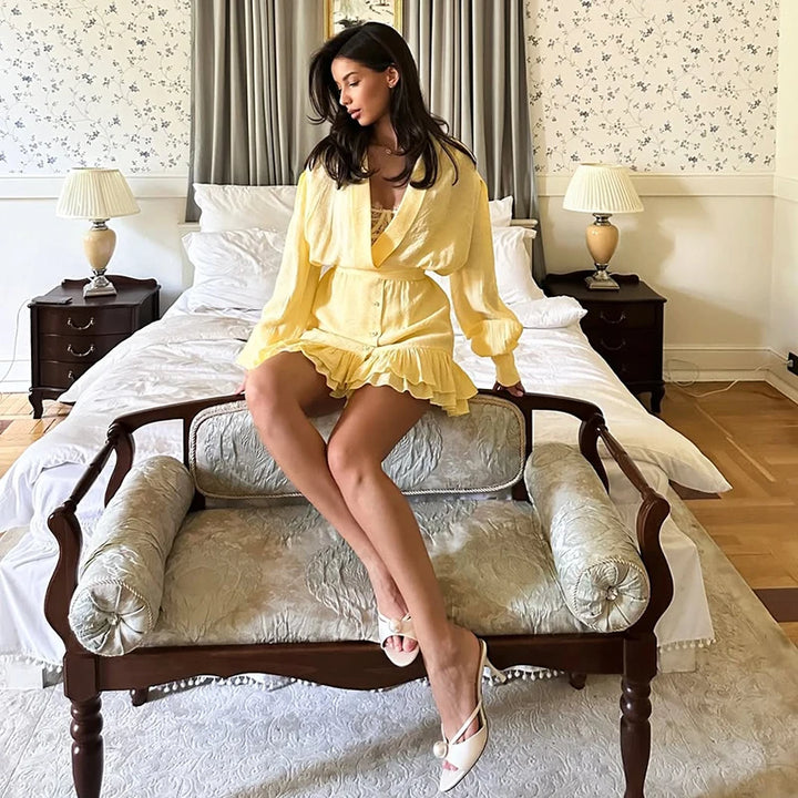 Woman in a yellow dress sitting on a bed in a bedroom.