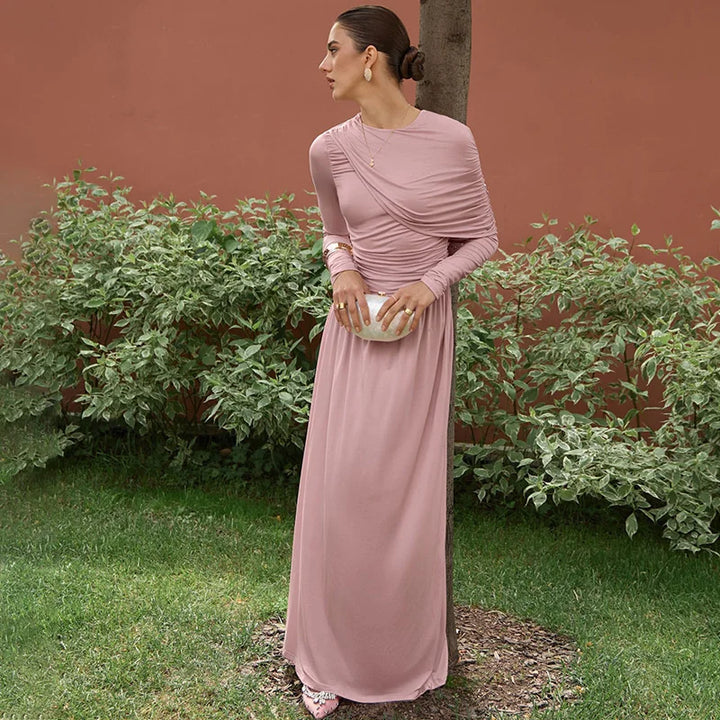 Woman in a pink dress standing outdoors against a red wall with greenery.
