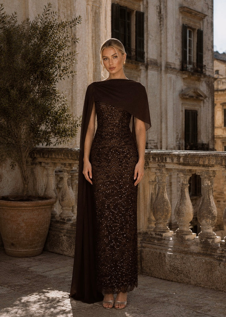 Woman in a dark dress with a cape standing on a balcony with classical architecture.