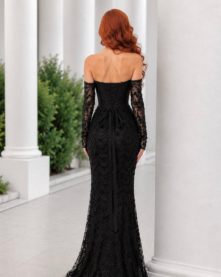 Woman wearing a black lace evening gown with long sleeves in an outdoor setting.