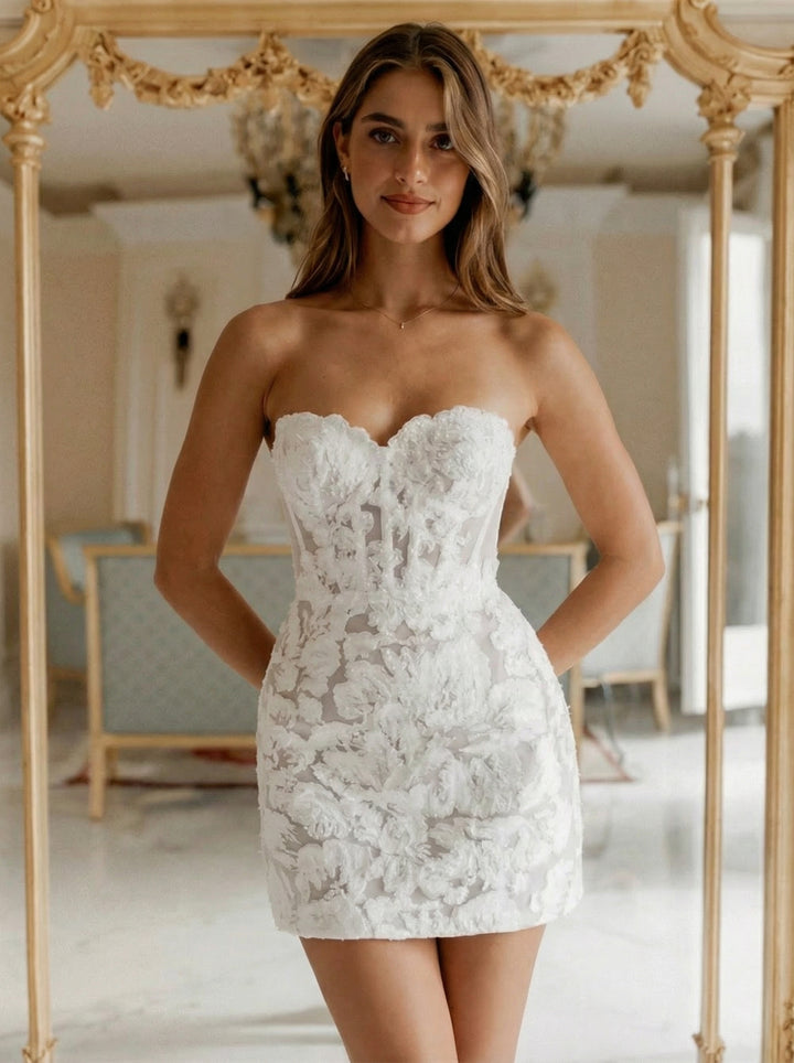Woman wearing a white lace dress standing in front of a decorative mirror.