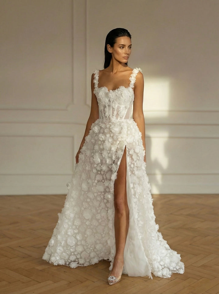 Woman wearing a white floral wedding dress with a high slit in a room with wooden flooring and white walls.