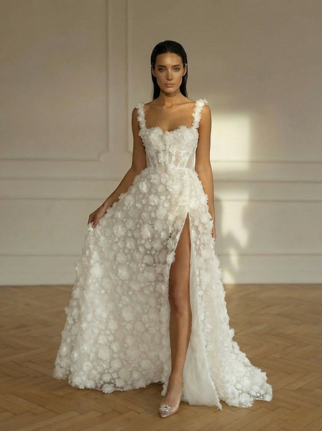 Woman wearing a white floral wedding dress with a high slit in a room with wooden floor and white walls.