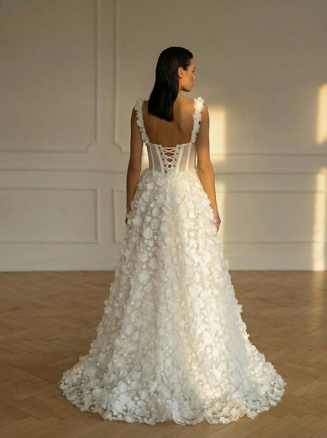 Woman wearing a white floral wedding dress in a room with wooden floor and white walls.