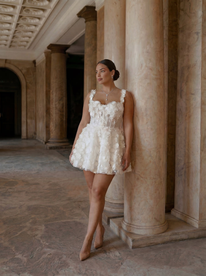 Woman in a white floral dress standing in an elegant indoor setting with columns.
