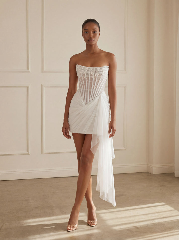 Woman wearing a white strapless dress against a neutral wall.