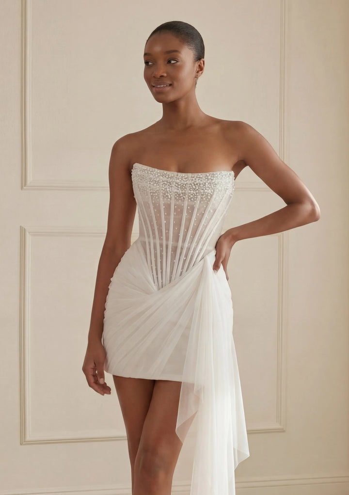 Woman wearing a strapless white dress with intricate detailing against a neutral background
