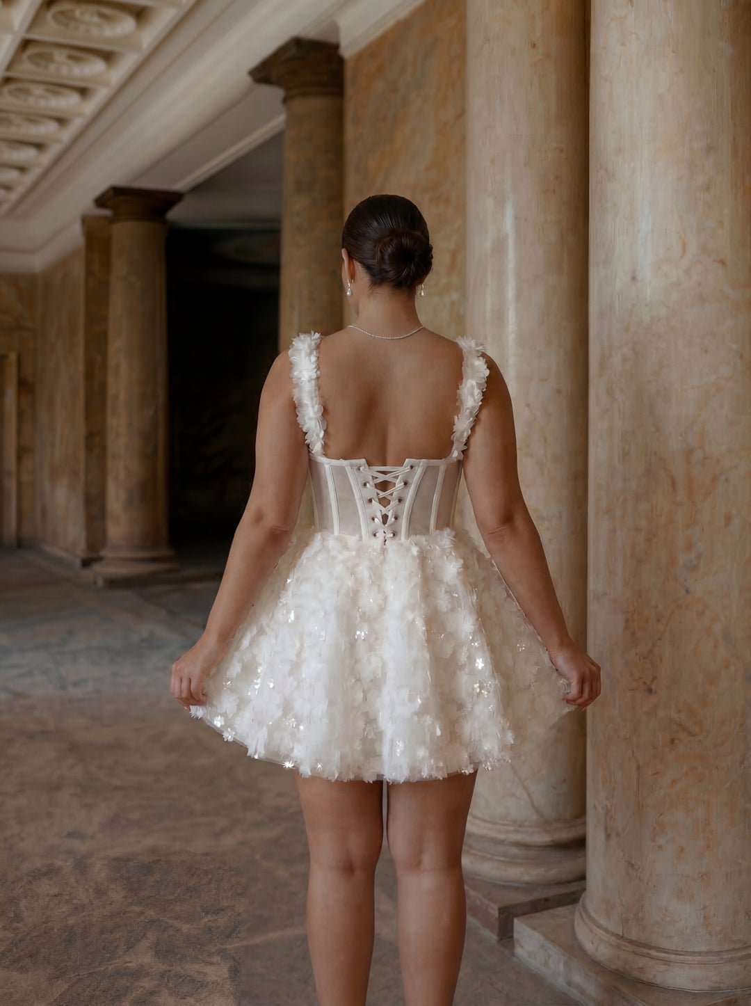 Woman in a white dress with floral details standing in an ancient architectural setting.