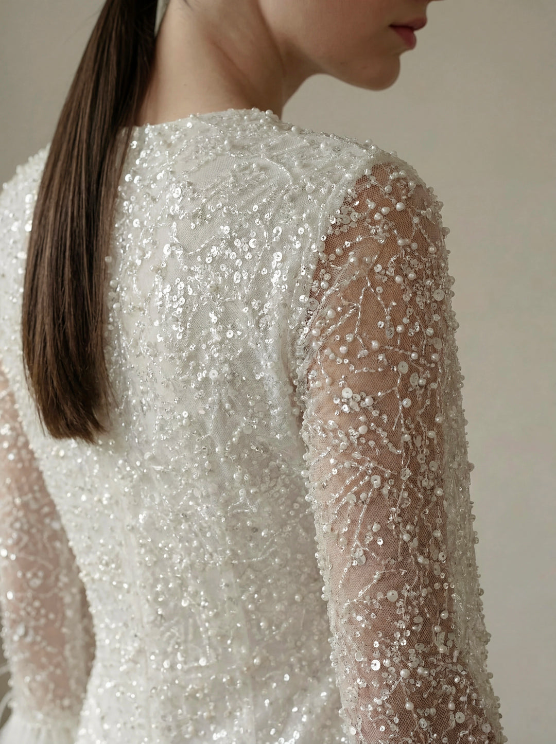 Close-up of a person wearing a white beaded dress with long sleeves.