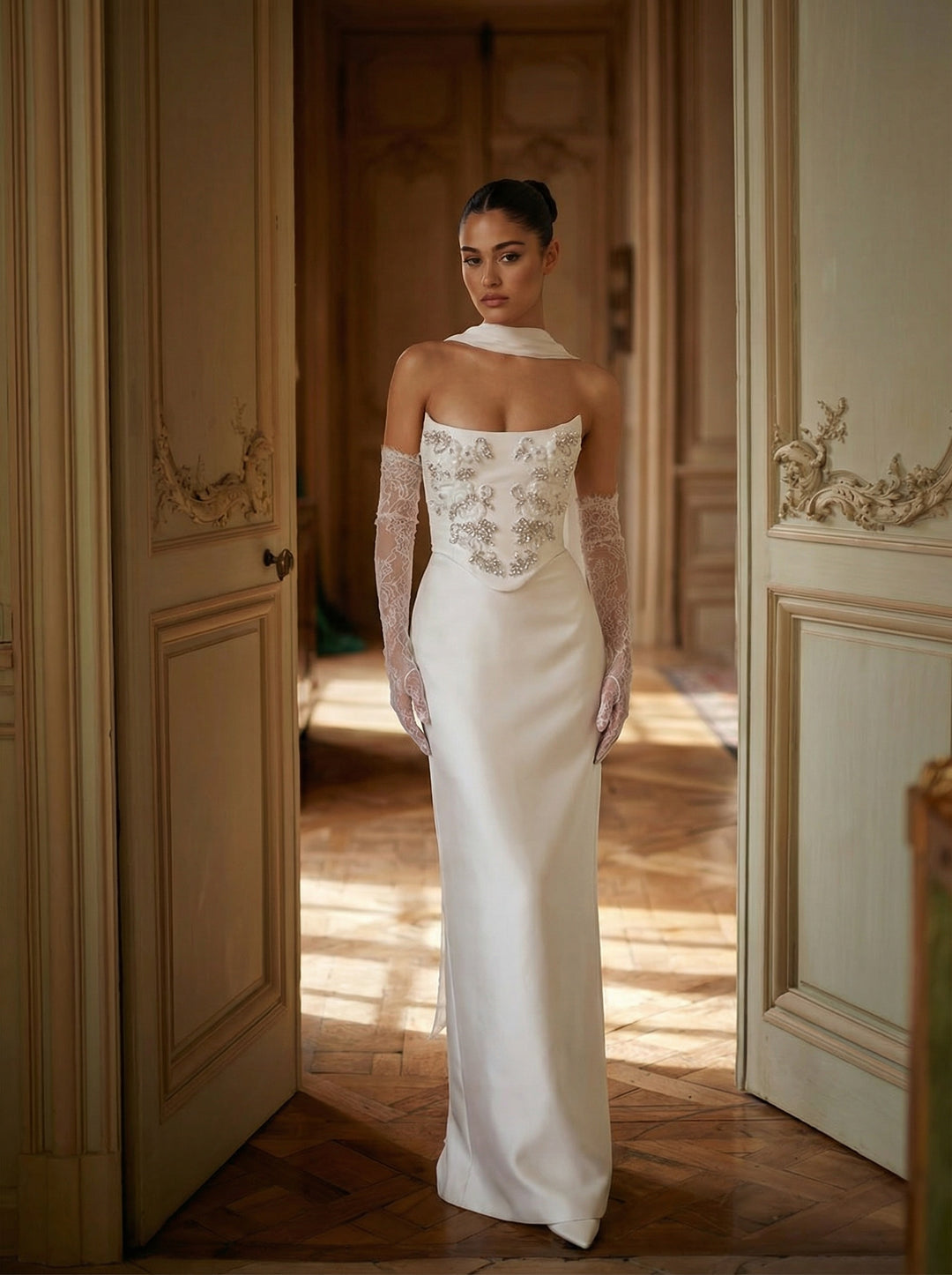 Woman in a white wedding dress with lace detailing standing in an elegant room.