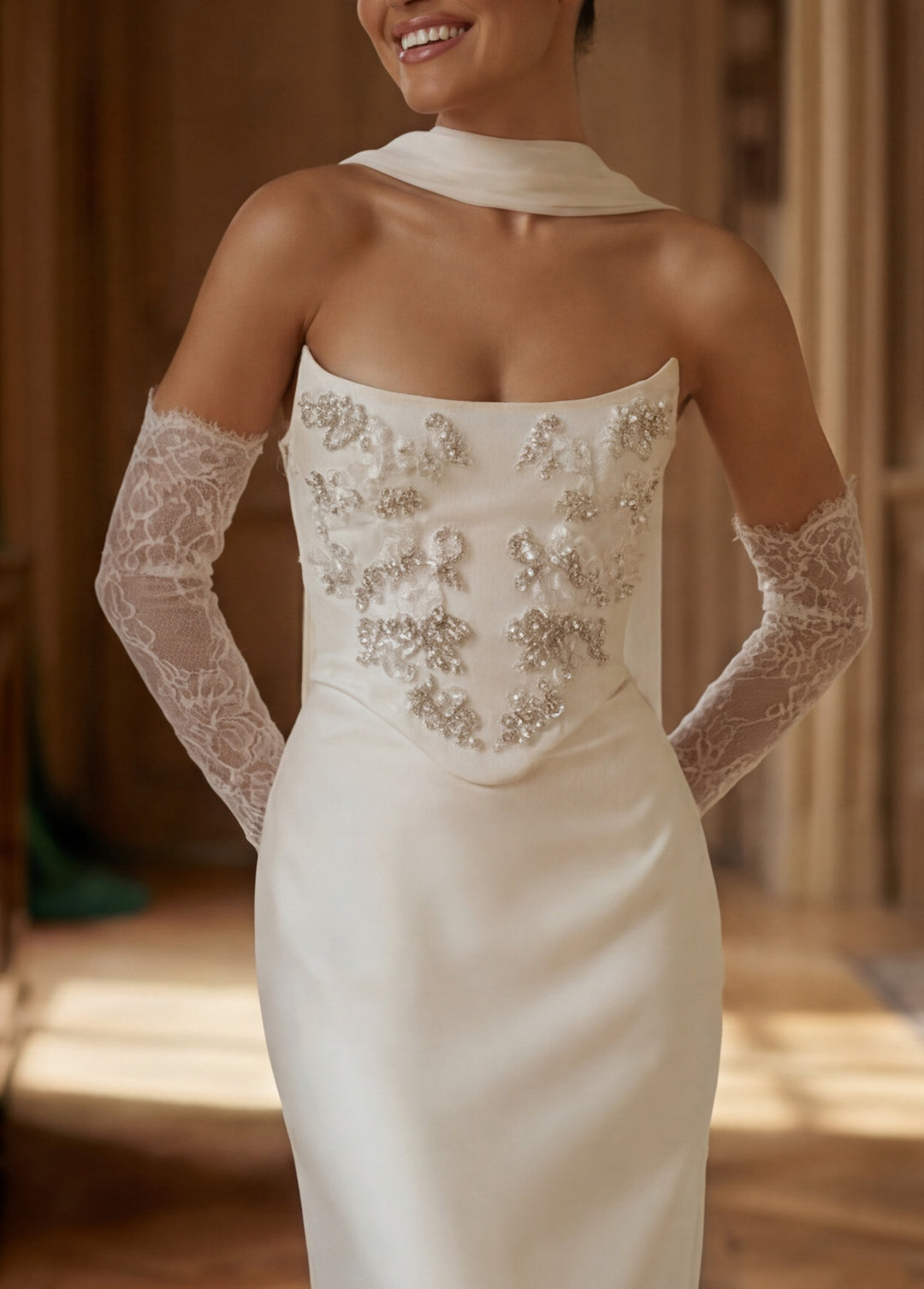 Woman wearing a white wedding dress with lace gloves indoors.