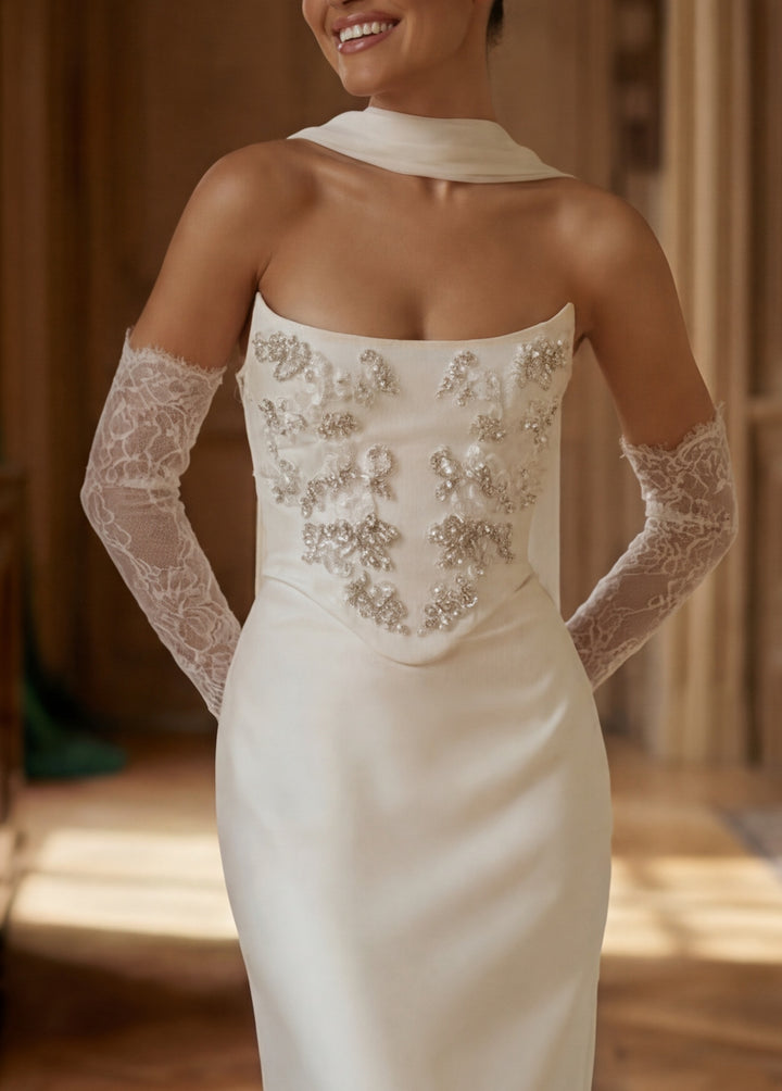 Woman wearing a white wedding dress with lace gloves indoors.