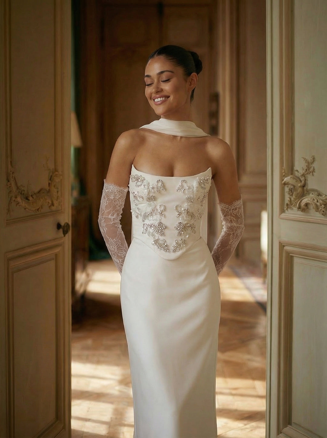 Woman in a white wedding dress with lace detailing standing in a doorway.