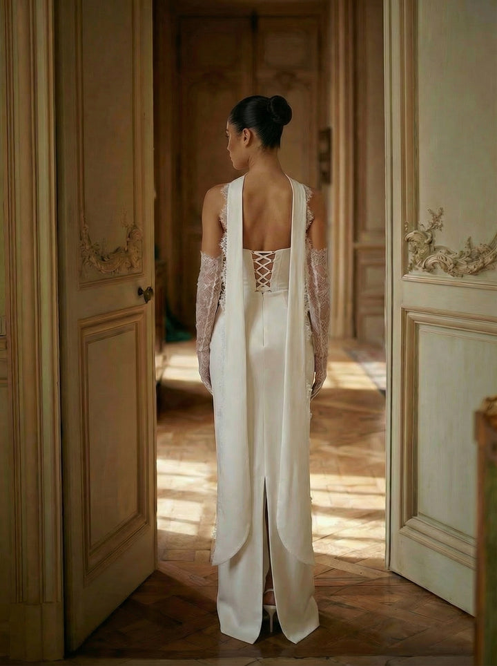Woman in a white outfit standing in a sunlit room with wooden floors and paneled walls.