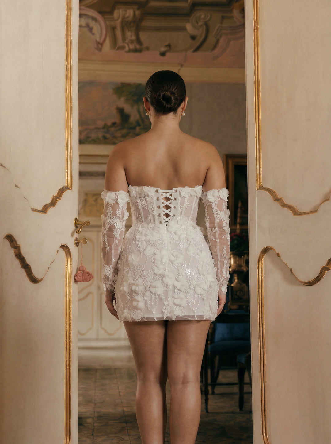 Person wearing a white lace dress standing in a room with decorative walls.