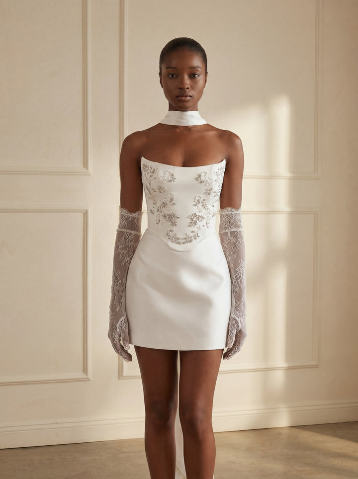 Woman wearing a white dress with lace details against a neutral wall.