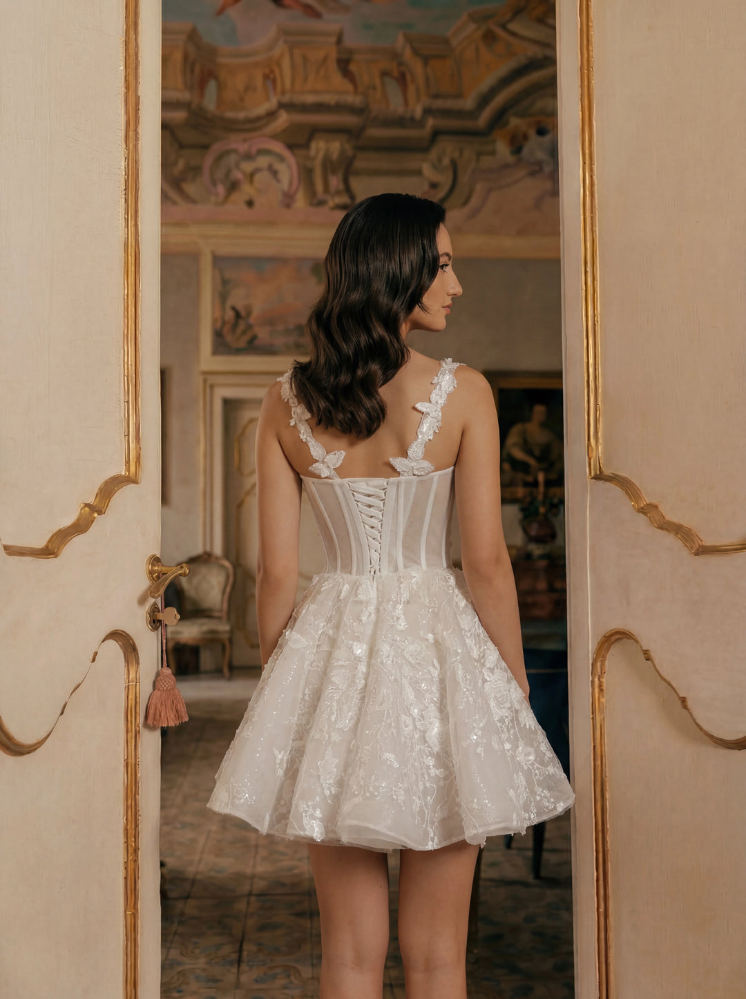 Woman in a white lace dress standing in a room with decorative walls.