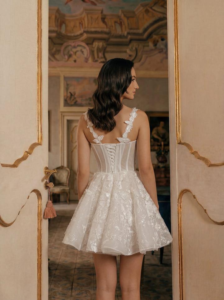 Woman in a white lace dress standing in a room with decorative walls.