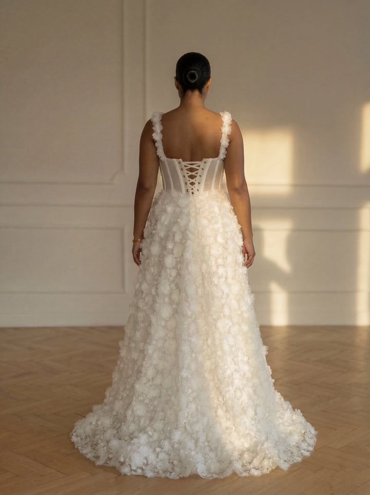 Woman wearing a white floral wedding dress in a softly lit room.