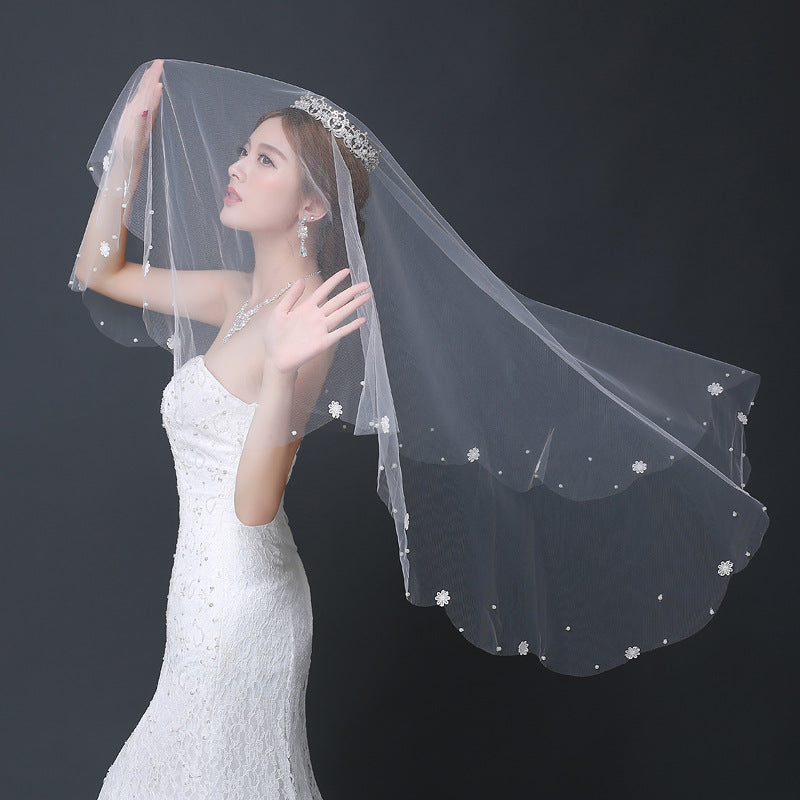 Woman wearing a white wedding dress and veil with floral details on a dark background