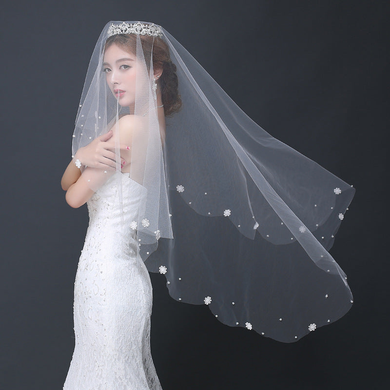 Woman wearing a white wedding dress and veil with floral details on a dark background