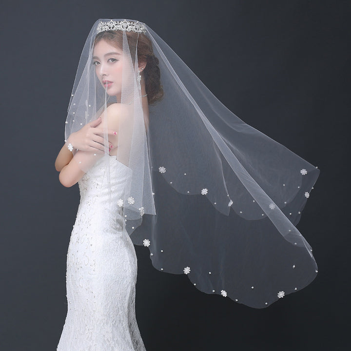 Woman wearing a white wedding dress and veil with floral details on a dark background
