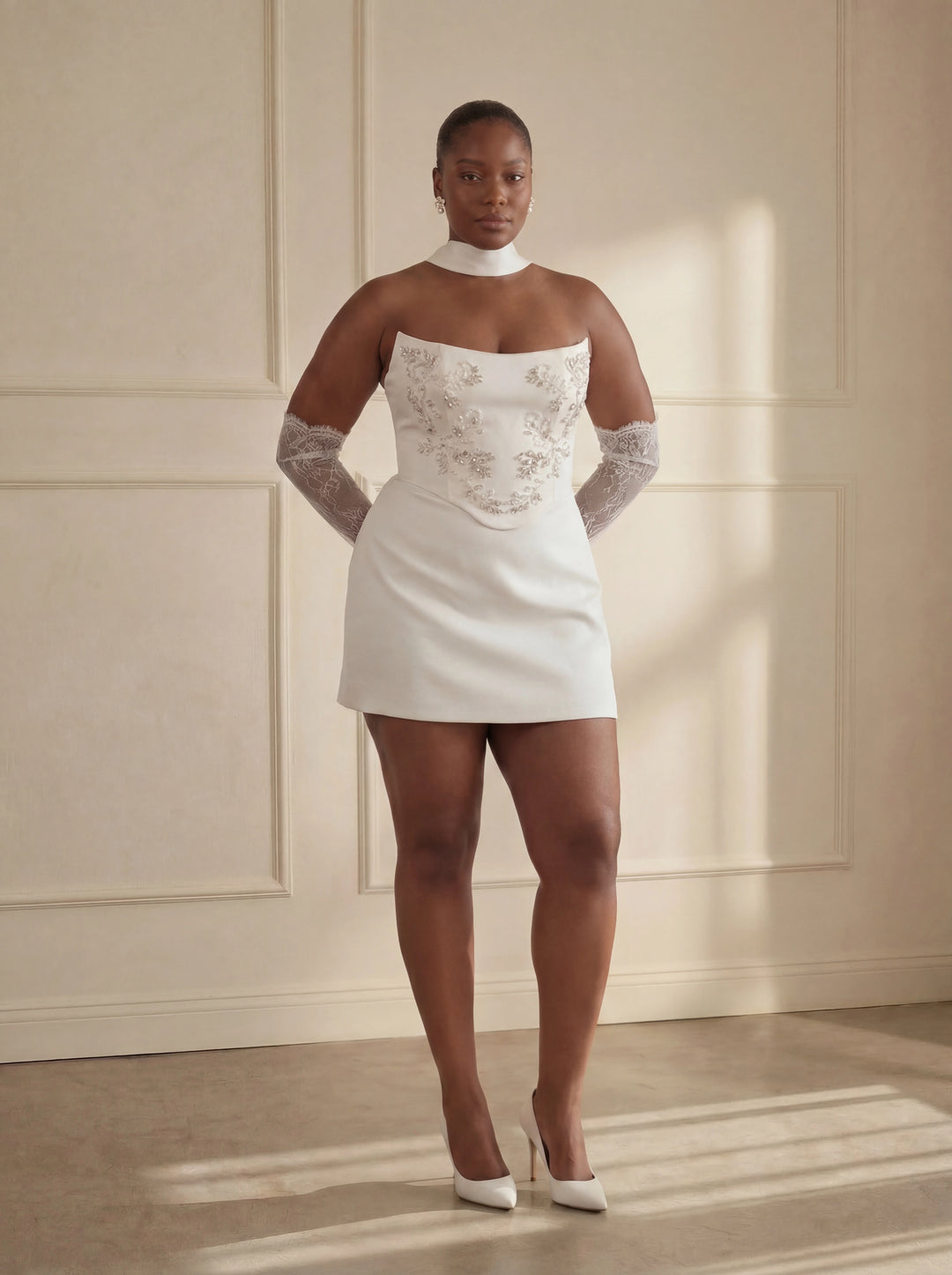 Woman wearing a white dress with lace details in a room with beige walls.