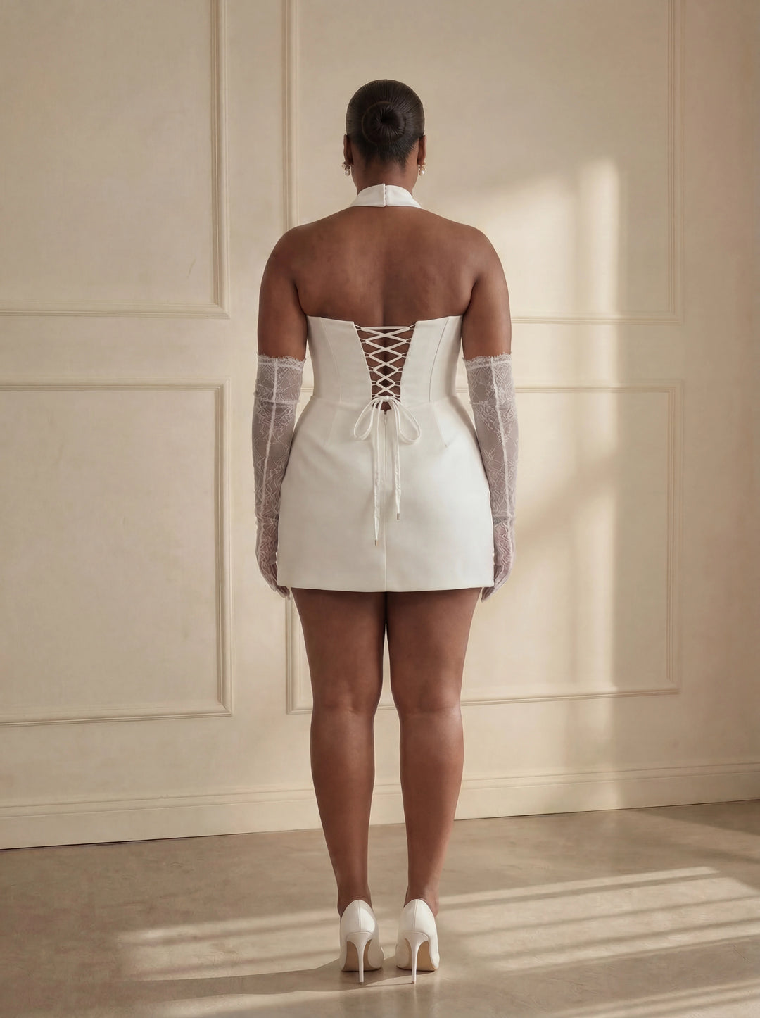 Woman wearing a white dress with sheer sleeves and lace-up back in a sunlit room.