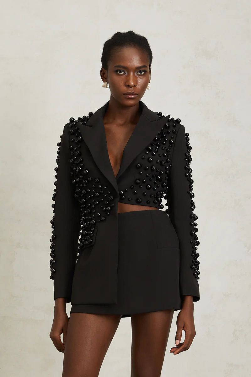 Woman wearing a black outfit with beaded details on a neutral background