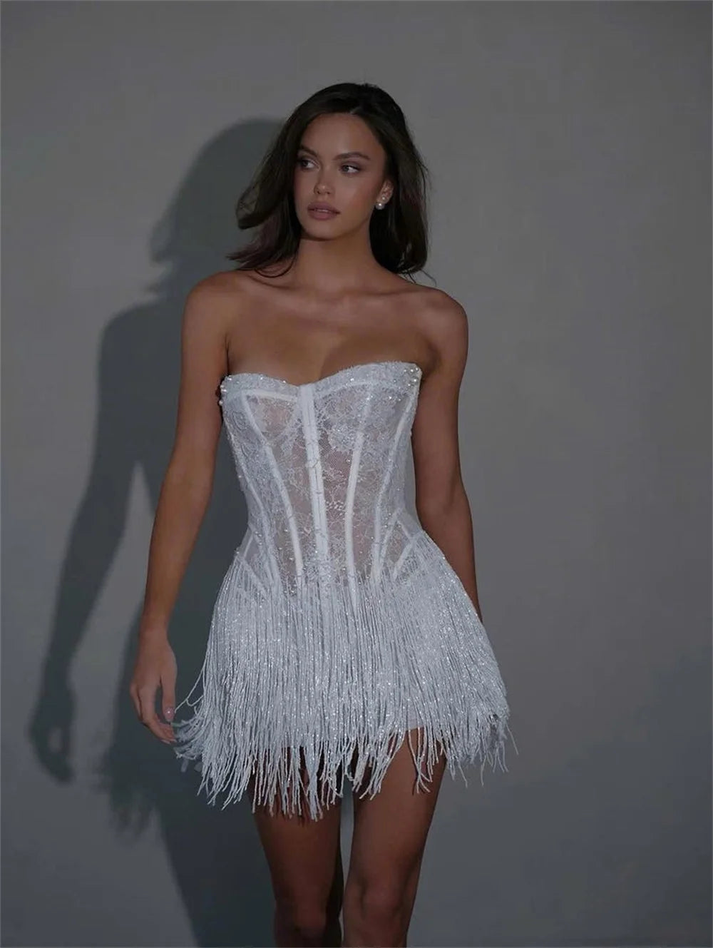 Woman wearing a white strapless dress with fringe details against a gray background