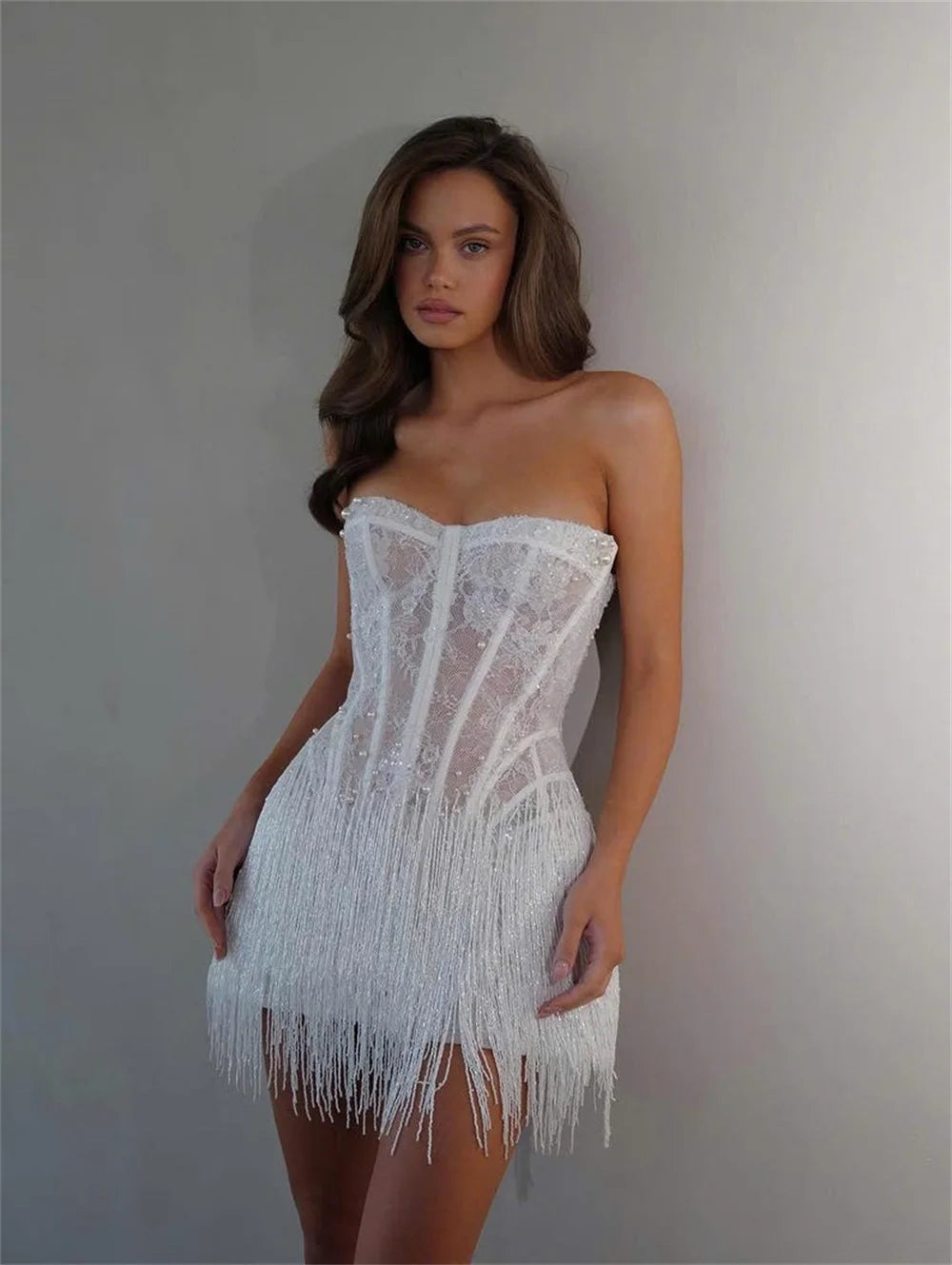 Woman wearing a white strapless dress with fringe details against a plain background