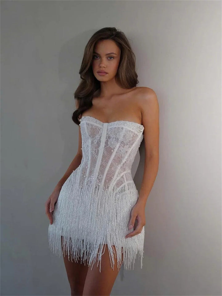Woman wearing a white strapless dress with fringe details against a plain background