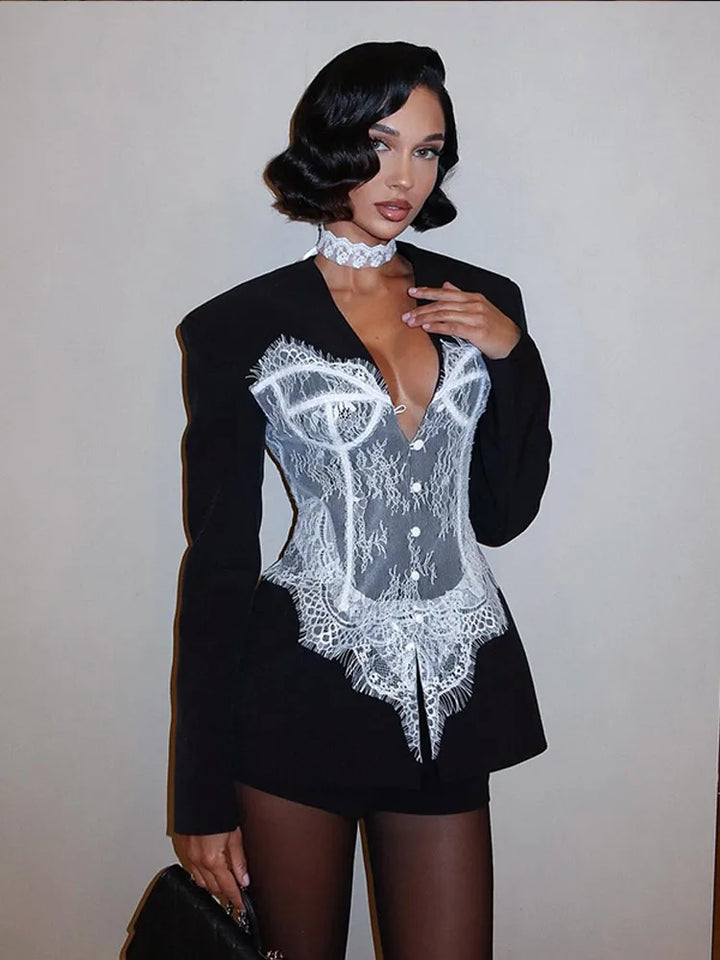Woman wearing a black blazer over a white lace top against a plain background