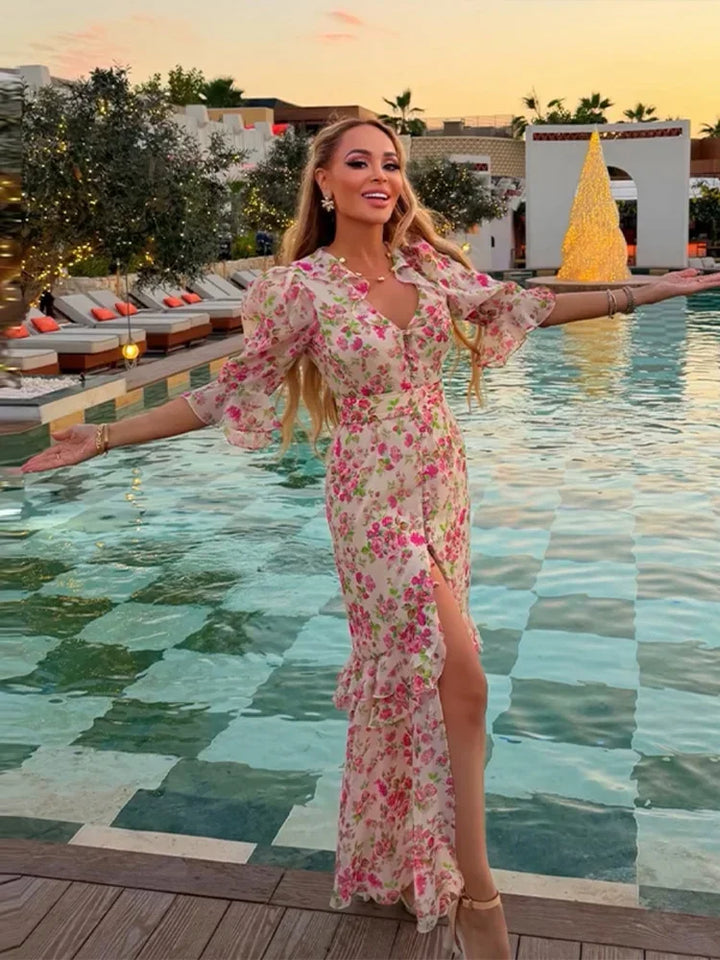Woman in a floral dress standing by a pool with a sunset background