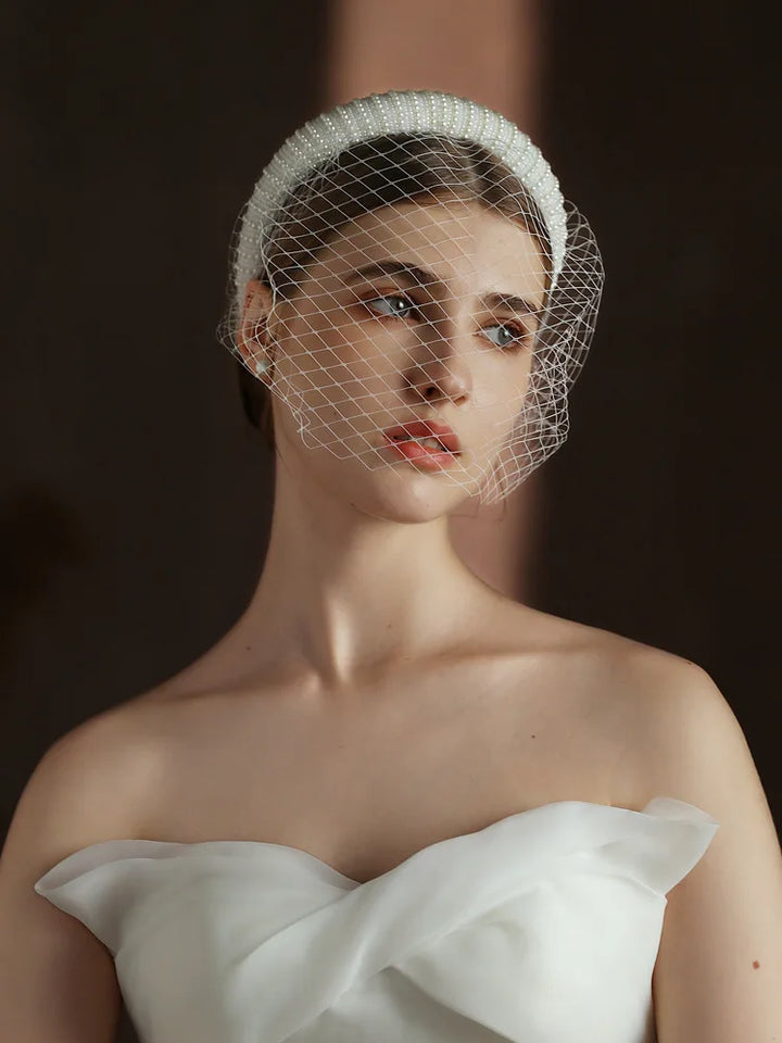 Woman wearing a white birdcage veil against a dark background