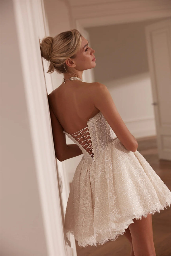 Woman in a white lace dress standing against a neutral wall.