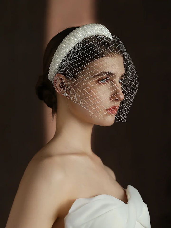 Woman wearing a white birdcage veil against a dark background