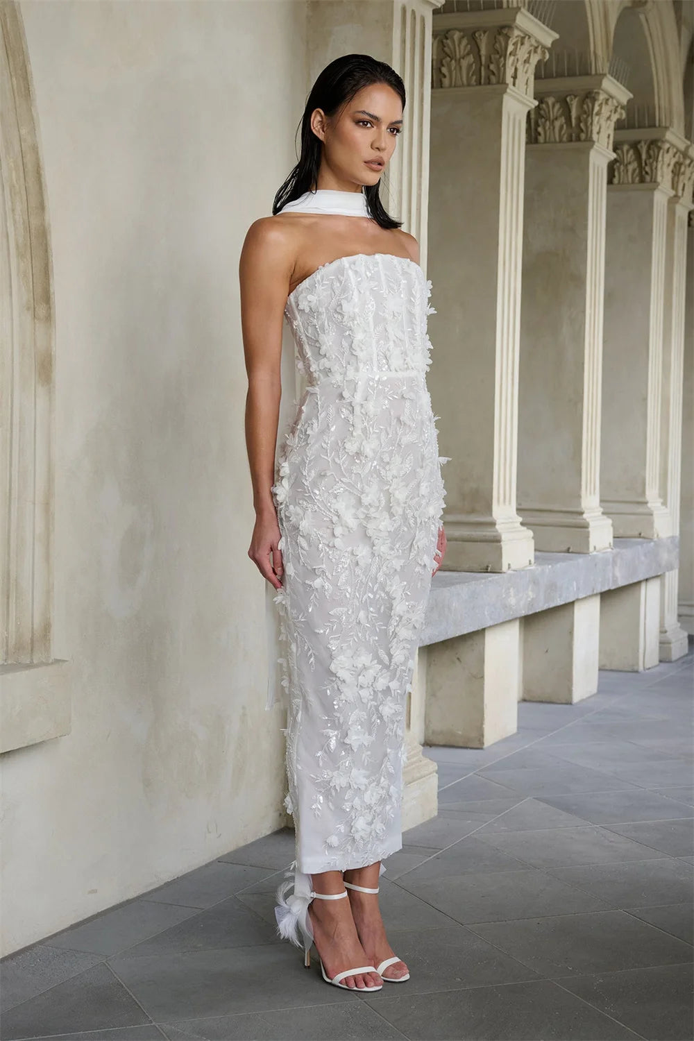 Woman in a strapless white floral dress standing in an elegant hallway.