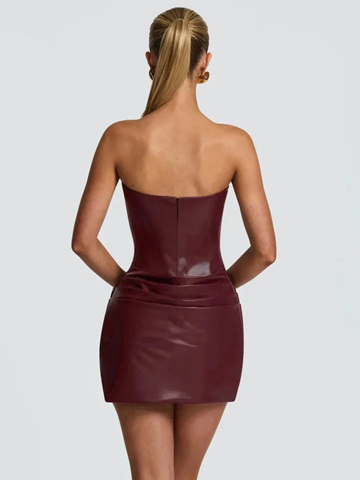 Woman wearing a strapless burgundy leather dress on a light gray background