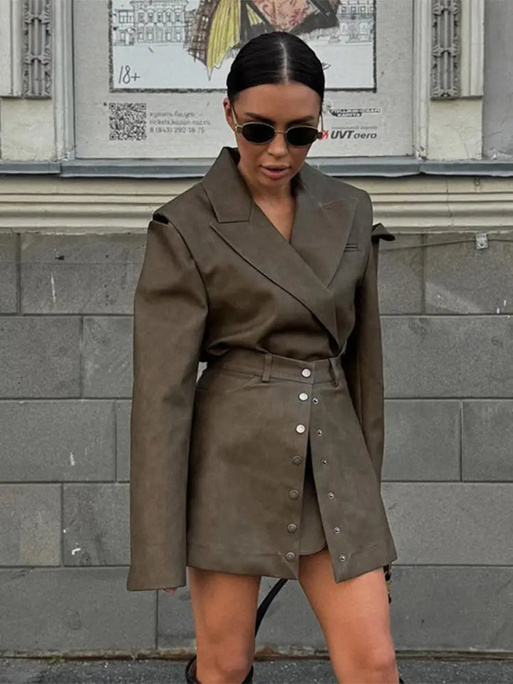Woman wearing a brown coat and skirt set against a gray wall.