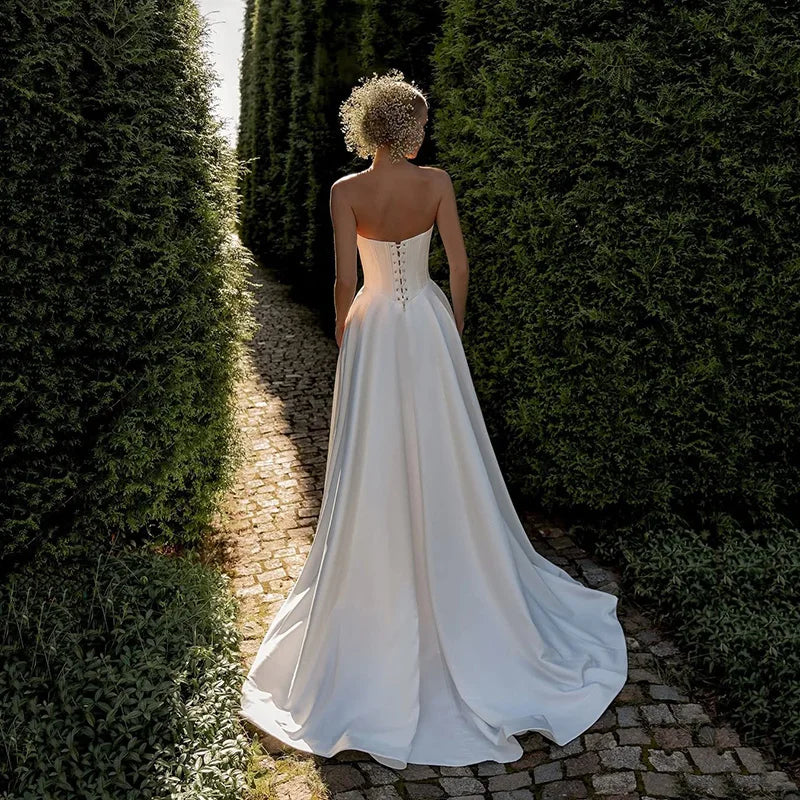 Woman in a white wedding dress standing between two rows of green hedges.